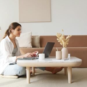 A woman uses a laptop at a coffee table in a cozy living room, embodying a relaxed work-from-home lifestyle.