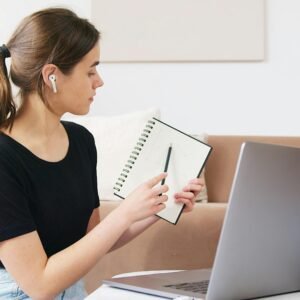 Female student engaging in online learning with laptop and notebook at home.